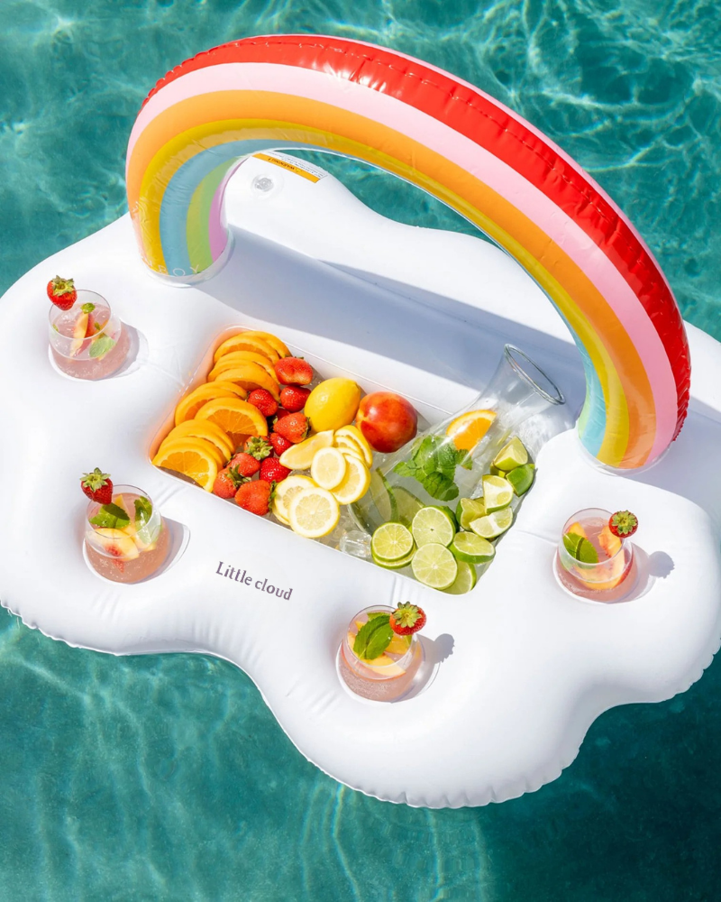 Little Cloud rainbow inflatable tray (cloud-shaped pool drink float) loaded with orange, lemon, lime and strawberry slices and drinks, floating in a blue swimming pool at a summer party.